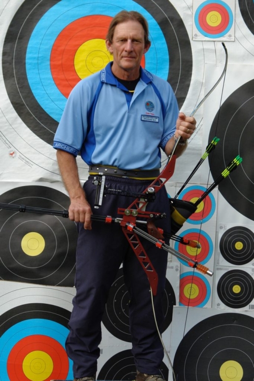 Garry stands in front of a target board, holding his bow and arrows.