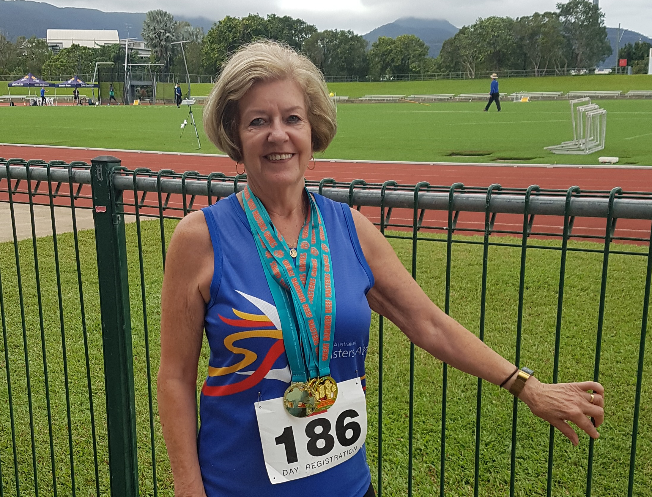 Woman stands in front of fence, wearing her medals