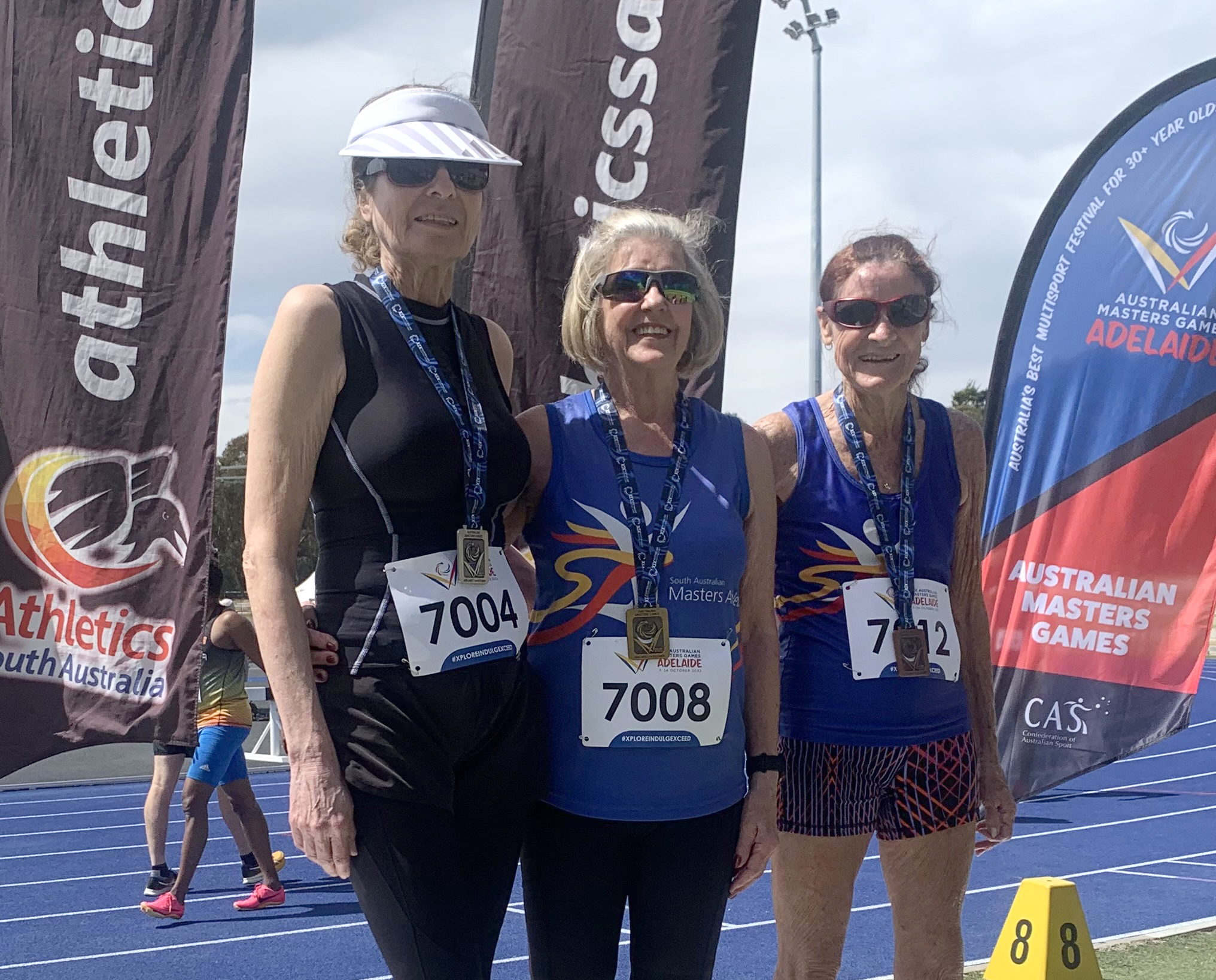 Three women stand on a podium on an athletics race track